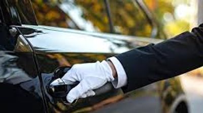 A person wearing white gloves opens a black car door.