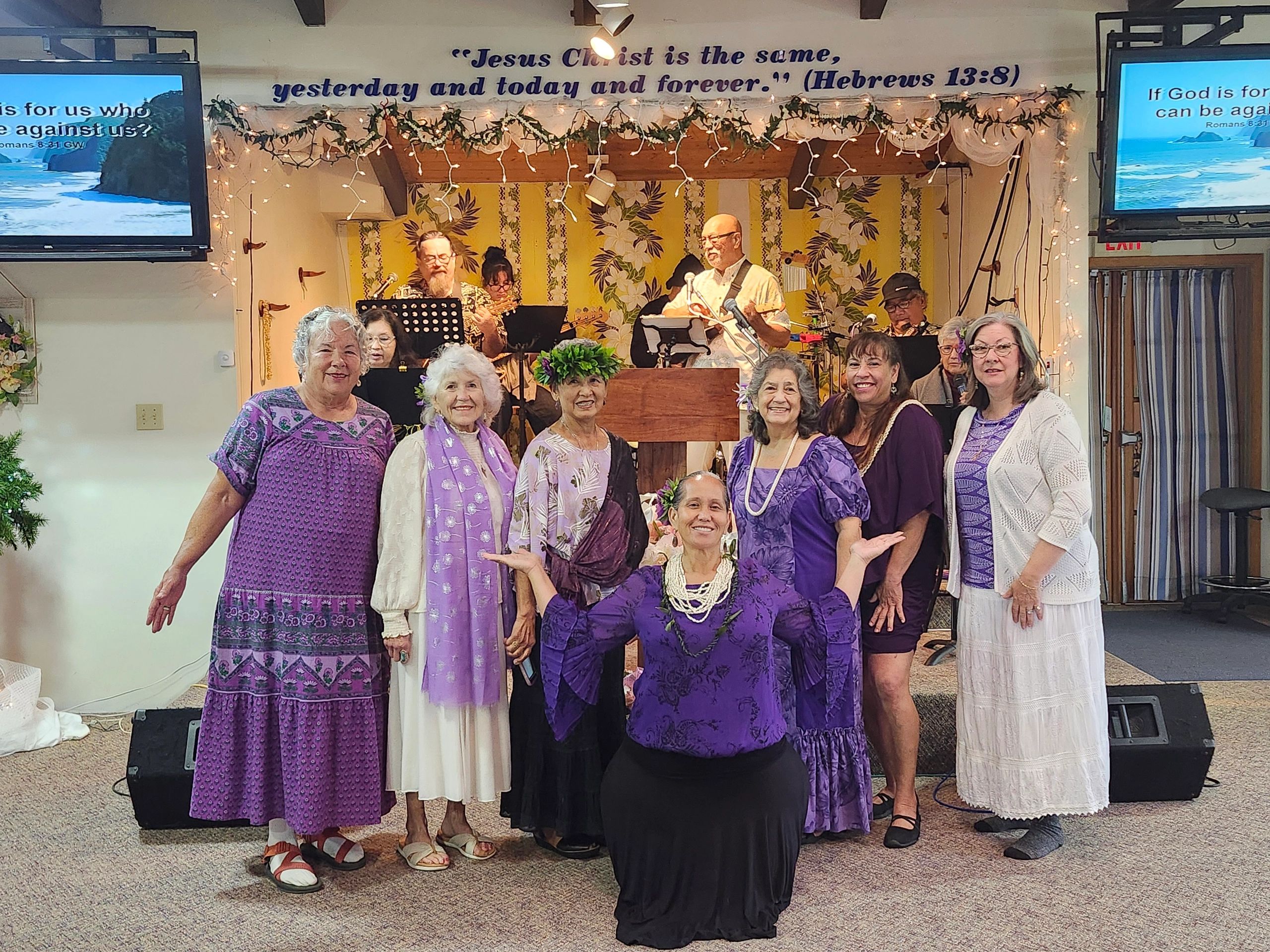 A joyful group of women in purple attire posing inside a decorated room with musicians.