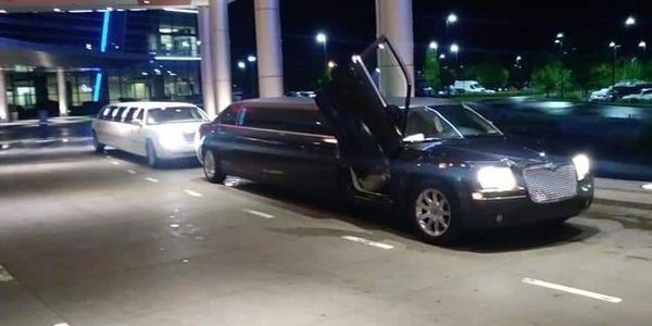 Two limousines parked under a well-lit entrance at night.