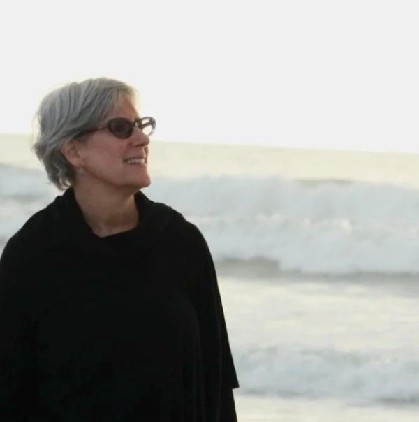 Older woman with glasses smiling by the beach.