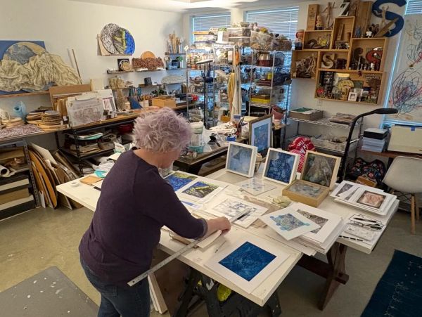 Artist working and measuring artwork in a cluttered studio.