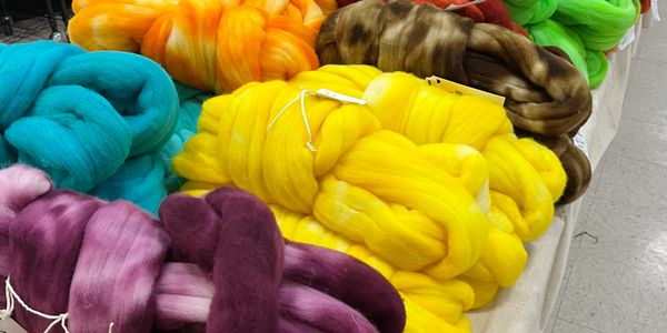 Colorful bundles of wool roving displayed on a table at a craft market.