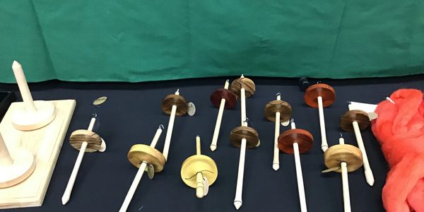 Various wooden drop spindles displayed on a black cloth with orange wool.