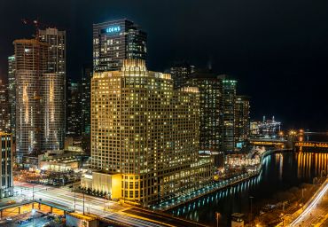 Cityscape at night with illuminated buildings by the water.