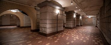 Empty underground brick corridor with arches and lights.