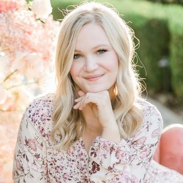 Woman in floral dress sitting on a pink chair, smiling gently.
