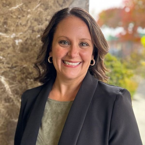 Smiling woman in a black blazer with a natural background.