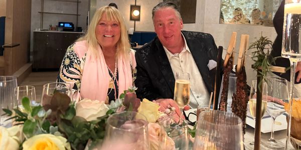 A smiling couple enjoying a dinner with flowers and drinks on the table.