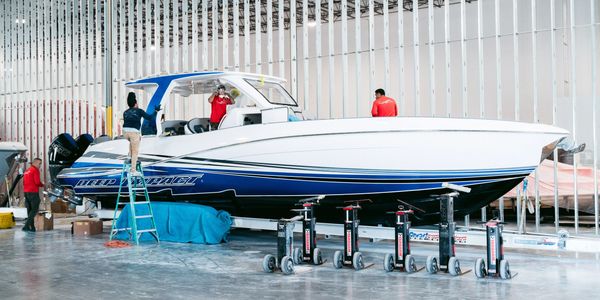 A sleek white and blue speedboat inside a large indoor facility with workers around it.