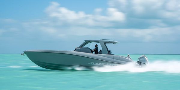 A sleek speedboat cruising on clear turquoise waters under a partly cloudy sky.