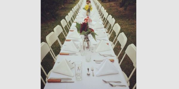 Long outdoor dining table set with white chairs and floral centerpieces.