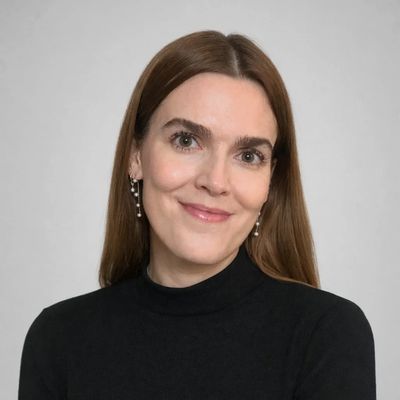 Smiling woman with long brown hair in black top against a plain background.