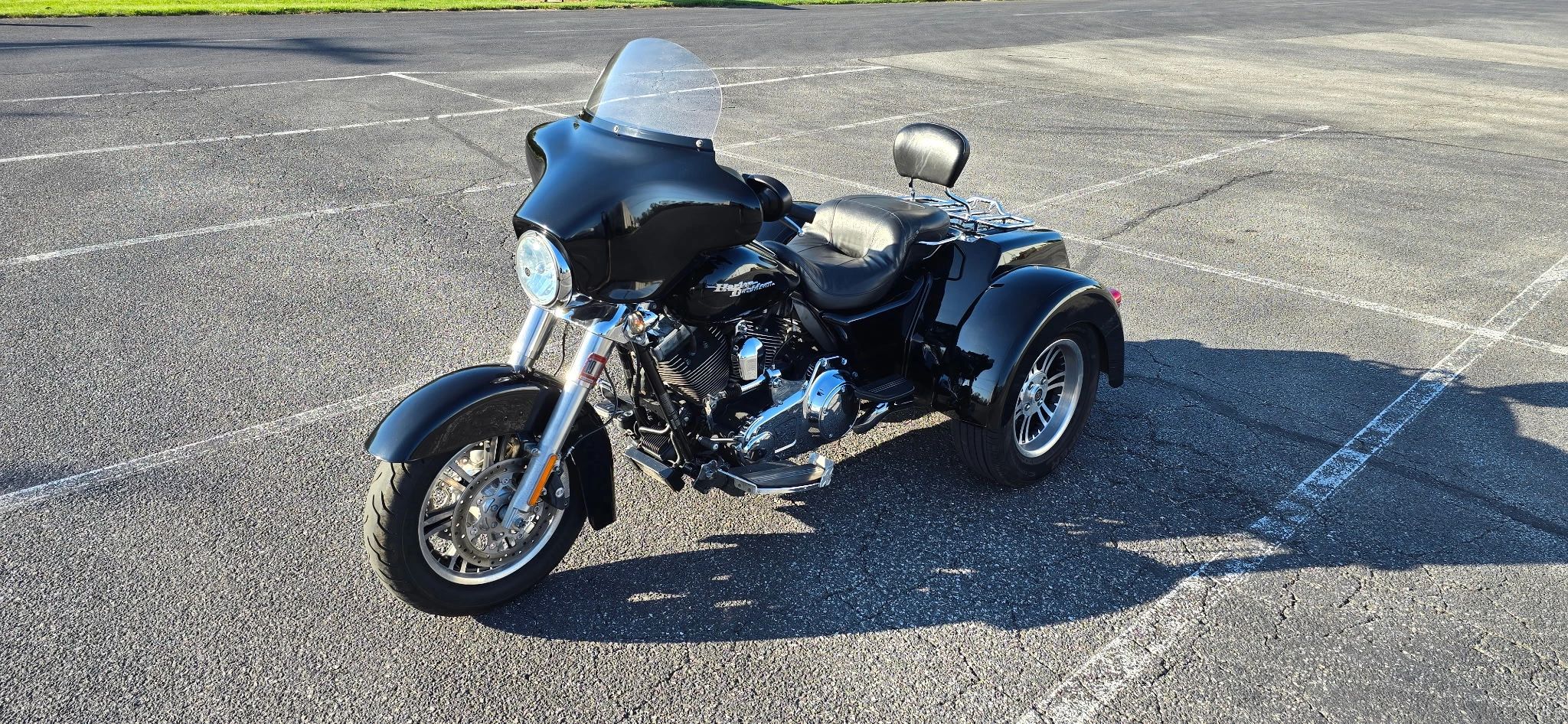 A black Harley-Davidson trike motorcycle parked in an empty lot on a sunny day.
