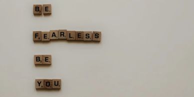 Scrabble tiles spell out 'BE FEARLESS BE YOU' on a plain background.