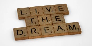 Wooden Scrabble tiles spell out 'LIVE THE DREAM' on a white background.