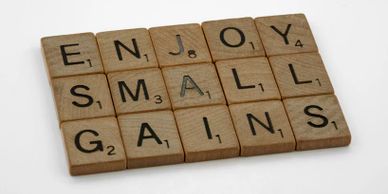 Scrabble tiles spelling 'Enjoy small gains' on a white surface.