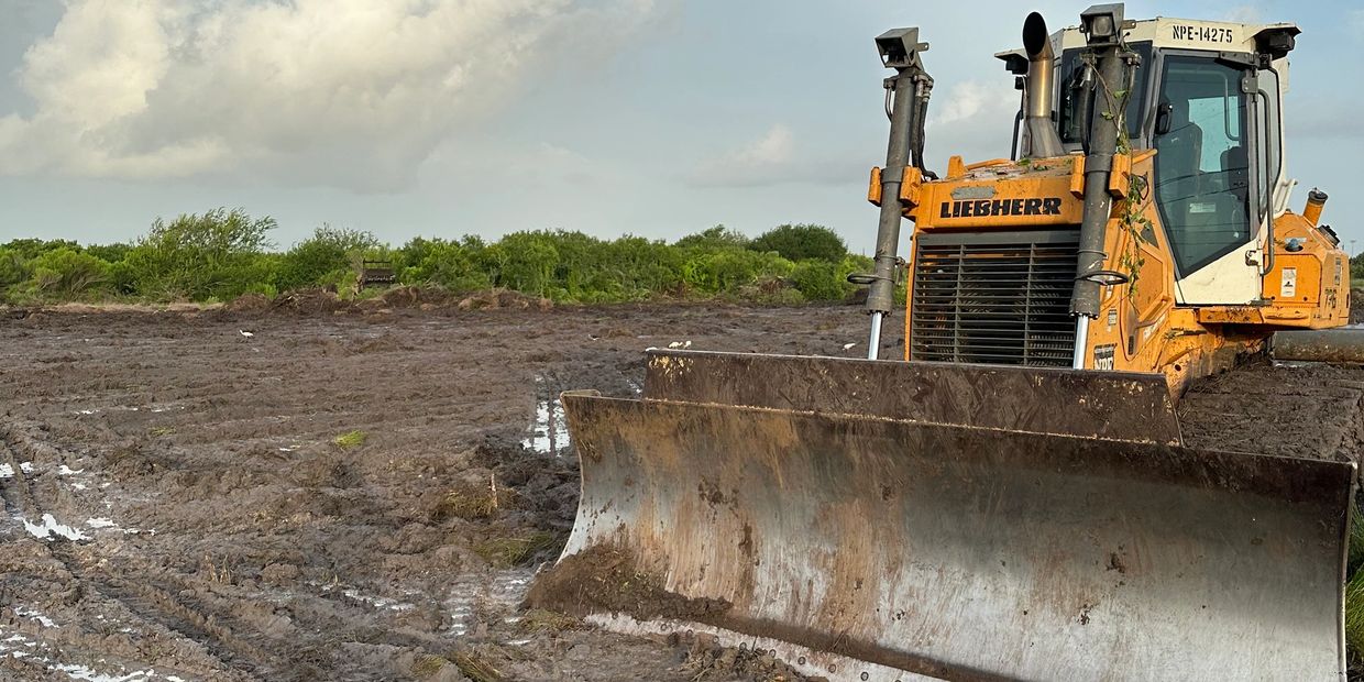 A yellow Liebherr bulldozer on muddy land under a cloudy sky.