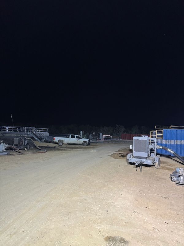 Nighttime industrial site with trucks and equipment on dirt ground.