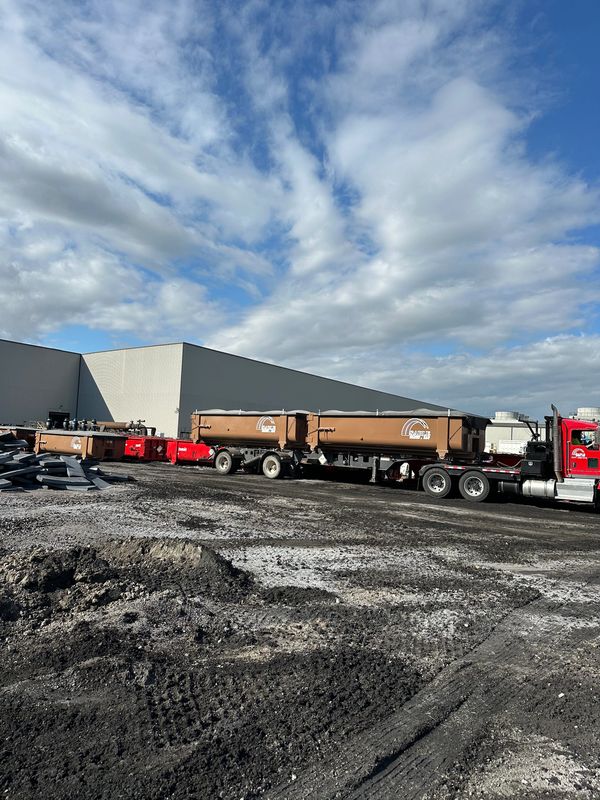 Large trucks parked on a dirt lot near an industrial building under a partly cloudy sky.