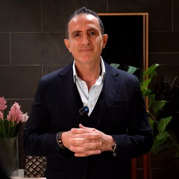 Man in a suit standing in front of a mirror, smiling confidently.