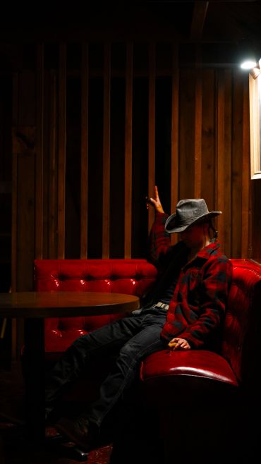 Person in a cowboy hat sitting on a red sofa in dim light.