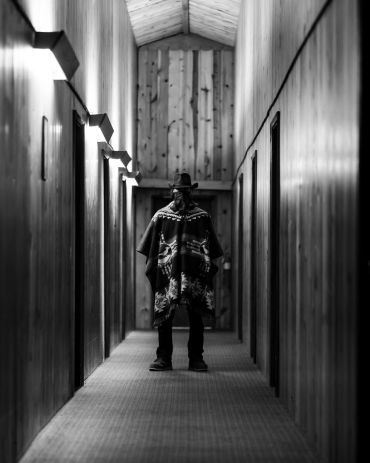 Man in a poncho standing in a wooden hallway.