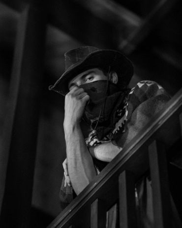 Man in cowboy hat and bandana at railing.