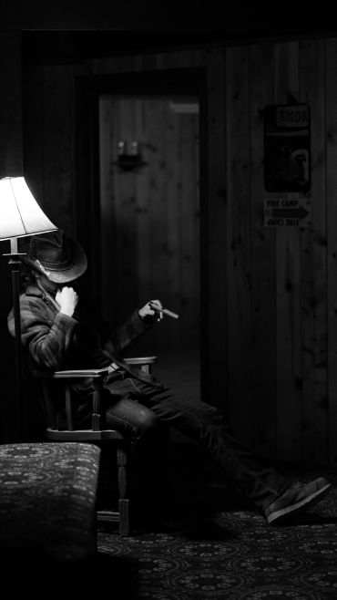 Man in cowboy hat sitting in dimly lit room.