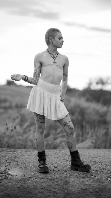 Person in a skirt and boots posing outdoors.