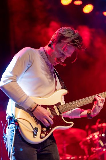 Guitarist passionately playing on stage with red lighting.