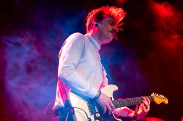 Musician playing electric guitar under colorful stage lights.