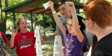 Children celebrating a cup-stacking game outdoors.