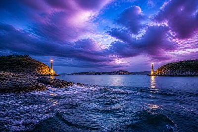Dramatic twilight seascape with lighthouses on rocky shores.