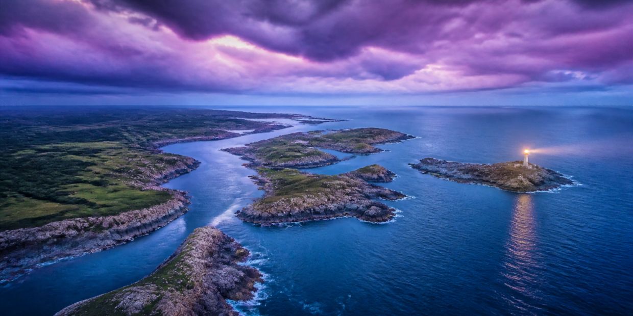 A coastal scene with a lighthouse on an island under dramatic purple skies.
