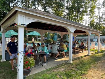 People enjoying a sunny day under a pavilion near a pool.