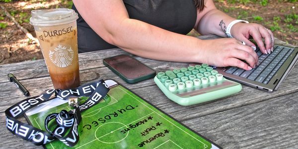 Person typing on a tablet with a green keyboard on a wooden table.
