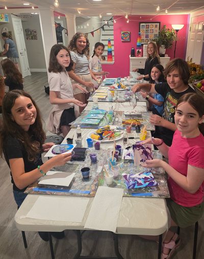 Group of kids painting together at a long table indoors.