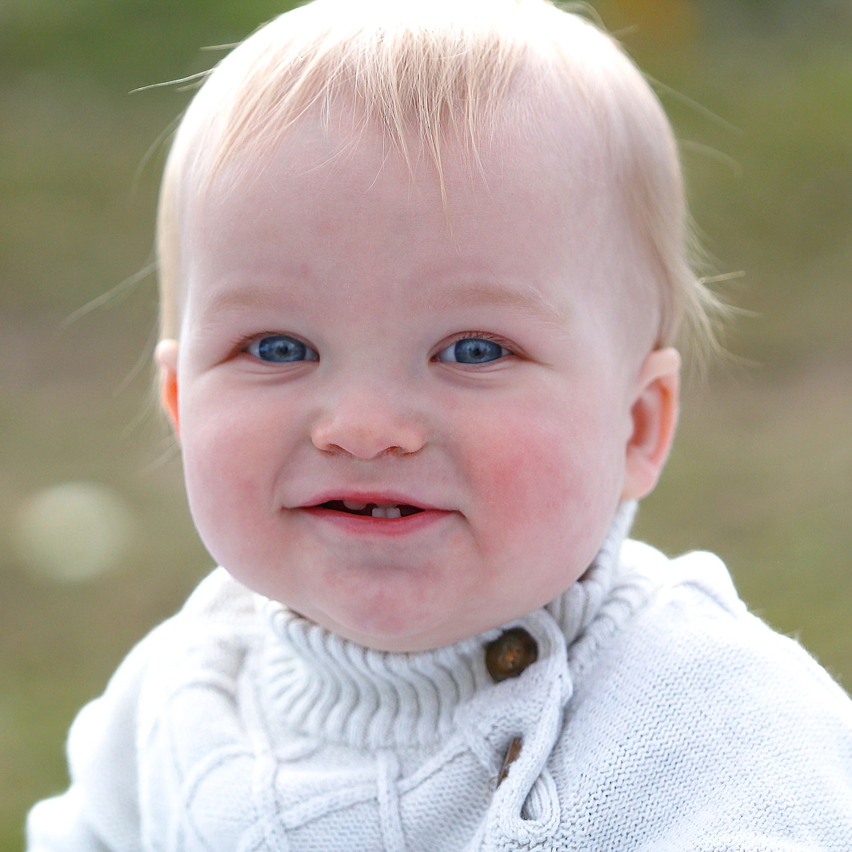 Close-up of a smiling baby with blue eyes in a white sweater.