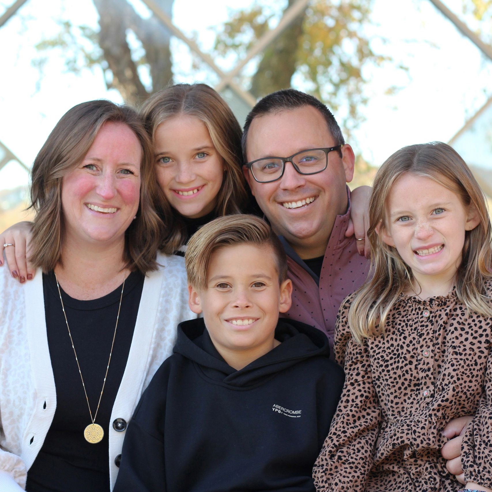 Smiling family posing together outdoors with trees in the background.