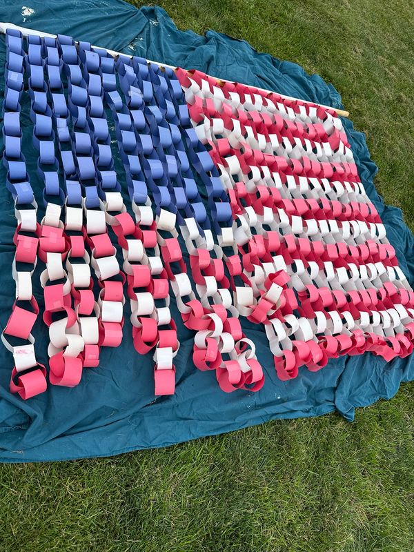 Handcrafted American flag made from red, white, and blue paper chains on a cloth.