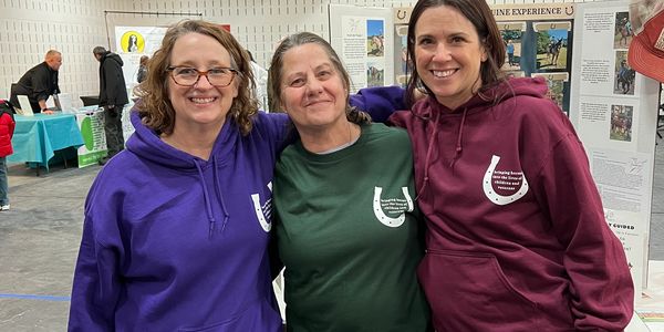 Three women smiling together wearing colorful hoodies with logos indoors.