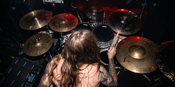 Drummer playing a drum set on stage with tattoos visible.