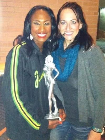 Two women smiling, one holding a trophy statue.