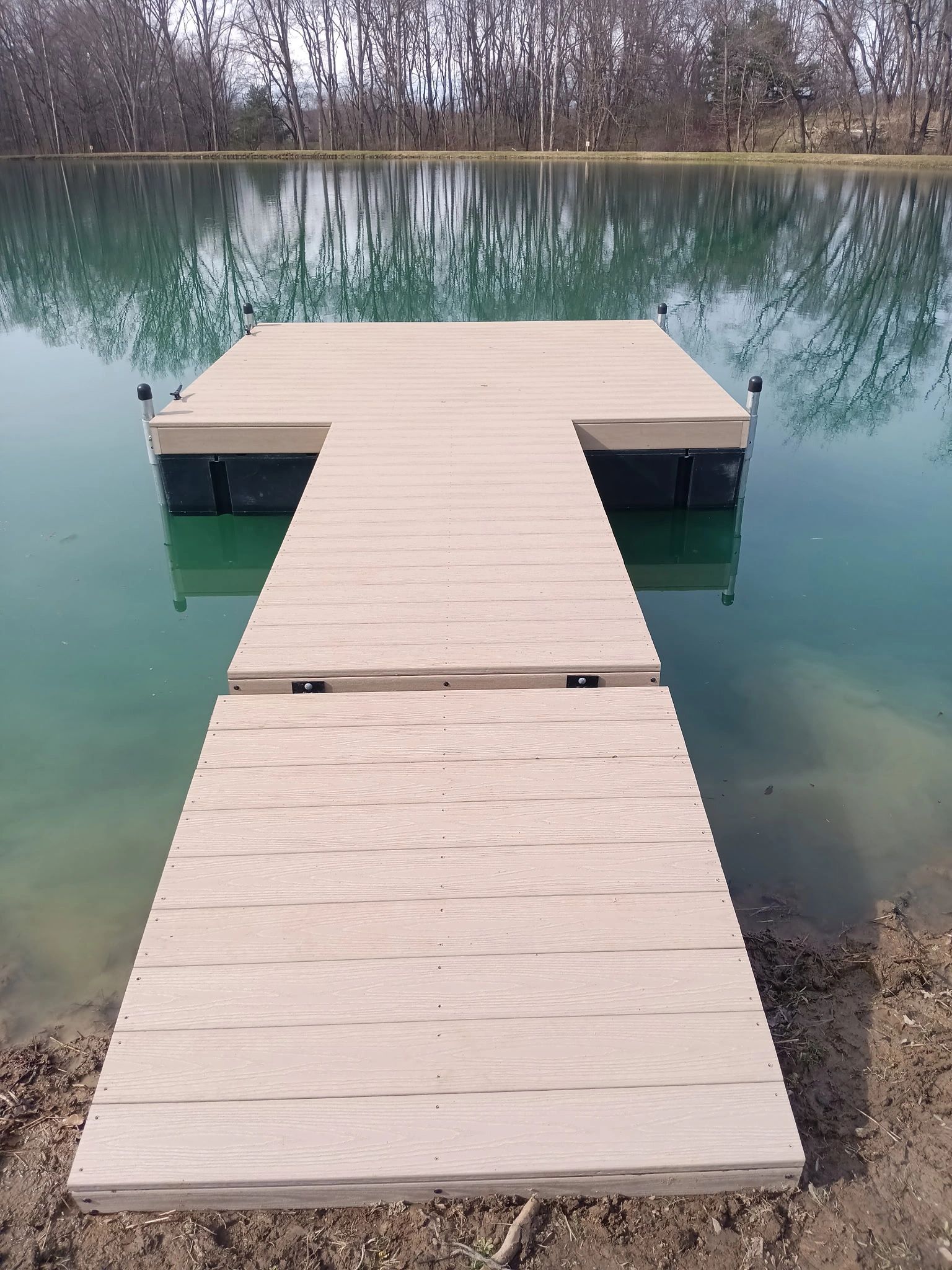 Floating T-shaped dock with composite decking on calm pond shoreline for low-maintenance waterfront 