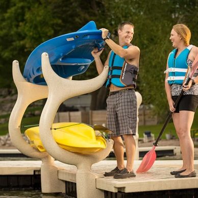 A man wearing a life jacket grabbing a kayak and a woman wearing a life jacket and holding a paddle. 