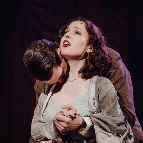 A man passionately embraces a woman who looks emotionally overwhelmed on stage.