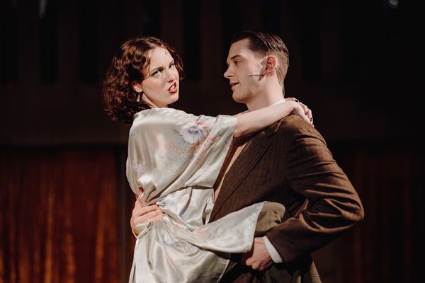 Actors performing a dramatic scene on stage, one holding the other.
