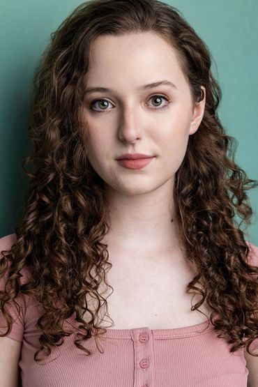 Young woman with curly hair and a pink top against a teal background.