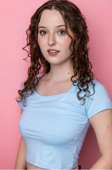 Young woman with curly hair poses against a pink background.