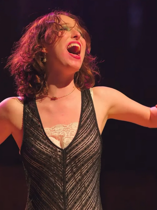 Woman passionately singing on stage with arms spread wide.